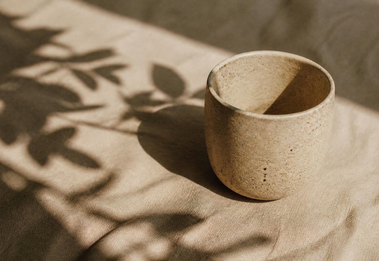 Taza de cerámica artesanal con sombra botánica sobre lino